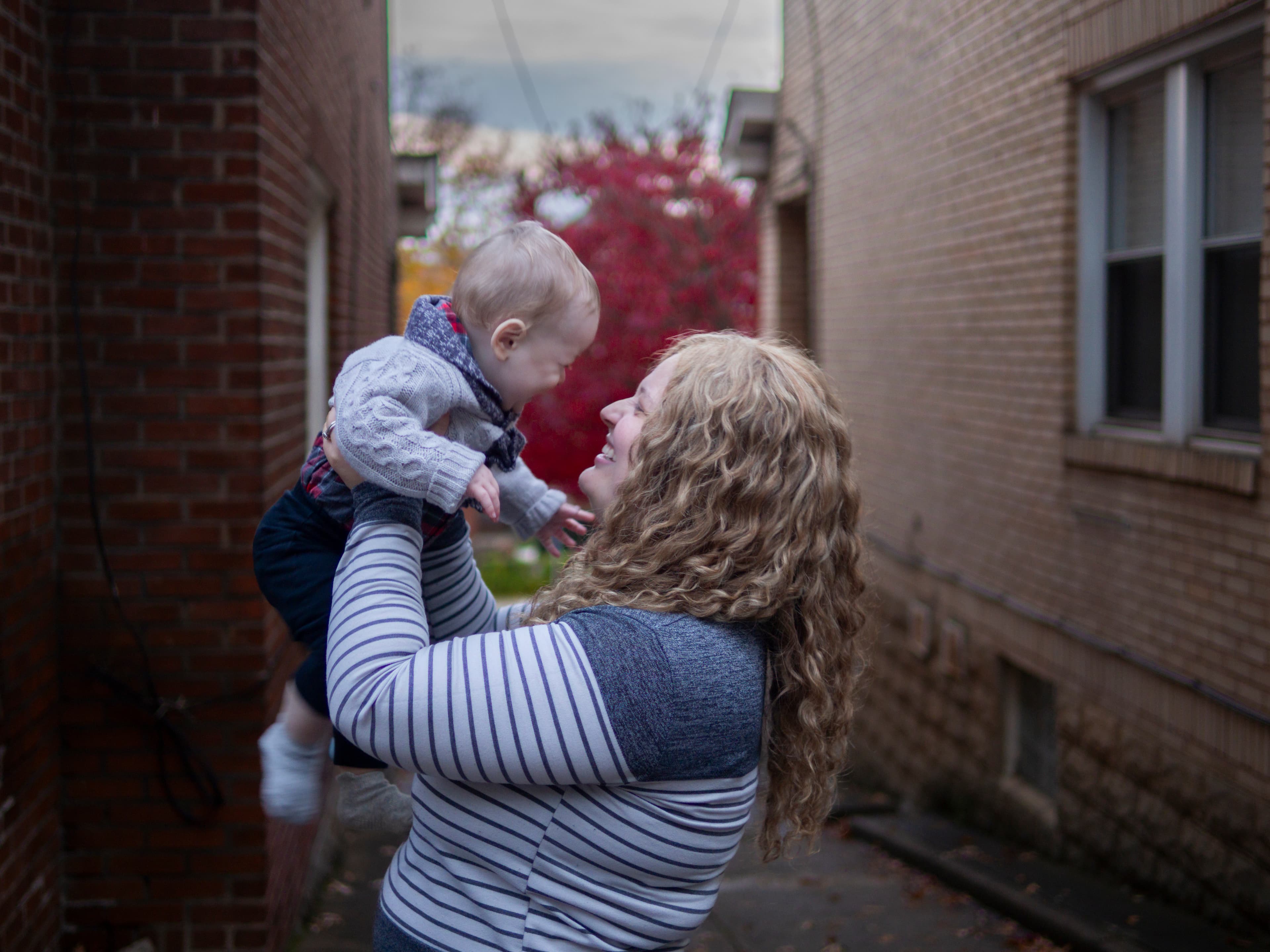 A mother smiling as she lifts her baby outdoors